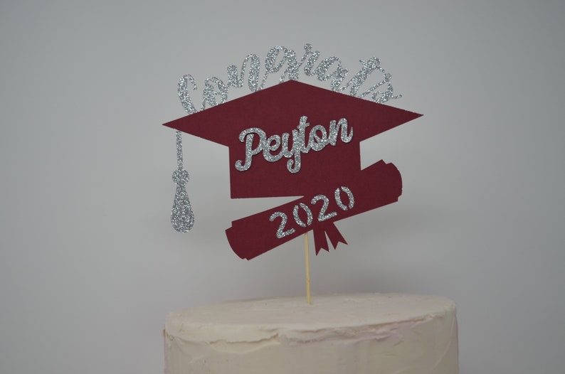 Puede incluir: Topper de pastel de graduaci&oacute;n de color burdeos en forma de gorro y diploma con detalles de purpurina plateada. El topper dice "Congrats Peyton 2020".