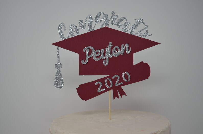 Puede incluir: Topper para pastel de graduaci&oacute;n en forma de gorro de color burdeos con letras de purpurina plateada. El topper dice "Congrats Peyton 2020".
