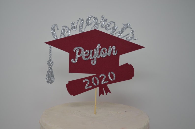 Puede incluir: Un adorno para pastel de graduaci&oacute;n rojo y plateado con un gorro de graduaci&oacute;n, un diploma y el texto "Congrats Peyton 2020".
