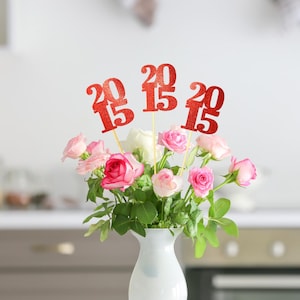 May include: A white vase filled with pink and white roses with red glitter 2015 graduation party decorations.