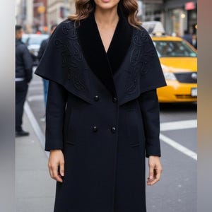 May include: A long, black coat featuring a cape-style collar. The collar is made of black velvet and has embroidered detailing. The coat has a double-breasted design and pockets. The background shows a city street with a yellow taxi.