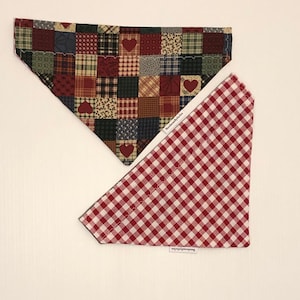 May include: Two dog bandanas, one with a red and white checkered pattern and the other with a patchwork pattern of red, green, blue, and brown squares with red hearts.