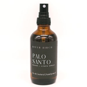 May include: A brown glass bottle with a black spray nozzle and label. The label reads "River Birch Palo Santo Room + Linen Spray" and "fresh | natural | hand poured".
