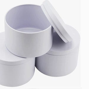 May include: Three white cylindrical containers with lids. The containers are stacked on top of each other. The lid of the top container is open.