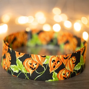 Könnte beinhalten: Ein schwarzes Stoffband mit einem sich wiederholenden Muster aus orangefarbenen Kürbisgesichtern und grünen Blättern.