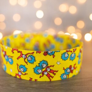 May include: A yellow fabric headband with a repeating pattern of blue and red figures from the book "The Cat in the Hat".