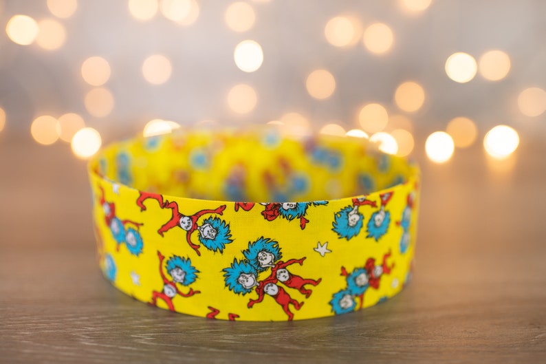 May include: A yellow fabric headband with a repeating pattern of blue and red figures from the book "The Cat in the Hat".