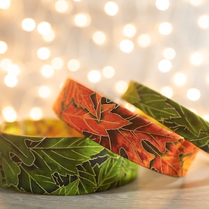 May include: Three fabric bands with a leaf pattern. The band on top is orange and brown with gold accents. The two bands underneath are green with gold accents.