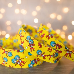 May include: Three yellow headbands with a repeating pattern of the characters from the book "The Cat in the Hat" by Dr. Seuss. The characters are wearing red and blue outfits and are dancing on a yellow background.