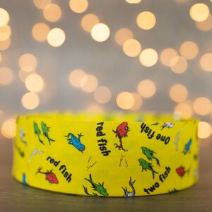 May include: A yellow fabric headband with a repeating pattern of red fish, blue fish, and green fish. The text "one fish, two fish, red fish, blue fish" is printed on the headband.