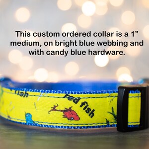 May include: A 1-inch medium dog collar with bright blue webbing and candy blue hardware. The collar features a yellow background with a red fish and blue bird illustration and the text "red fish".