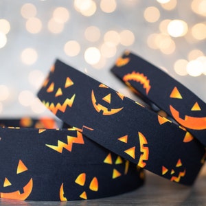 May include: Three black fabric headbands with a repeating pattern of orange jack-o'-lantern faces. The headbands are stacked on top of each other.