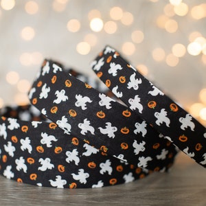 May include: Three rolls of black and white fabric with a pattern of white ghosts and orange pumpkins. The fabric is folded and stacked on a wooden surface.