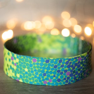May include: A green, blue and purple patterned fabric strap with a repeating circle design.