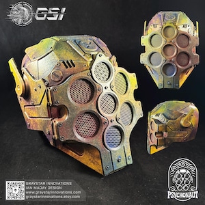 May include: A multi-colored, futuristic mask with a metallic finish. The mask features multiple circular vents and a complex, angular design. The color scheme includes shades of yellow, green, blue, and brown. The image also includes the text "GSI" and "PSYCHONAUT".
