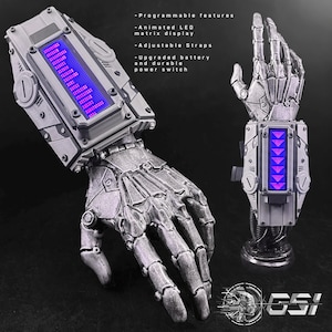 May include: A silver robotic hand with an animated LED matrix display, adjustable straps, and a durable power switch. The hand features programmable features and is designed with a futuristic aesthetic. The text on the display is blurry.