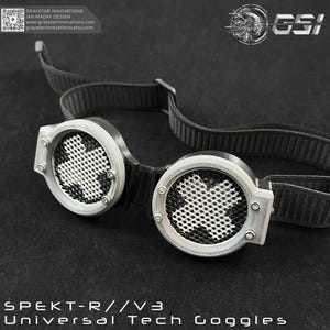 以下が含まれることがあります： レンズに十字模様が入った、シルバーと黒のユニバーサルテックゴーグル。ゴーグルには調節可能な黒いストラップが付いており、「SPEKT-R//V3 Universal Tech Goggles」と表示されています。