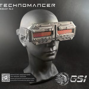 May include: A futuristic, silver-colored goggle-style mask with the text "NO FUTURE" above the lenses. The lenses have a red honeycomb pattern. The text "TECHNOMANCER" and "VERSION V1.0" are printed above the mask. The mask is displayed on a mannequin head.