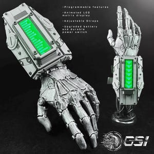 Puede incluir: Una mano robótica plateada con una pantalla de matriz LED animada y correas ajustables. El texto de la imagen dice: "Características programables, Pantalla de matriz LED animada, Correas ajustables, Batería mejorada e interruptor de encendido duradero."