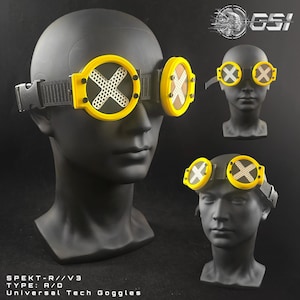May include: Yellow and black Universal Tech Goggles with a white cross design on the lenses. The goggles are displayed on a black mannequin head. The text "SPEKT-R//V3 TYPE: A/O Universal Tech Goggles" is visible.