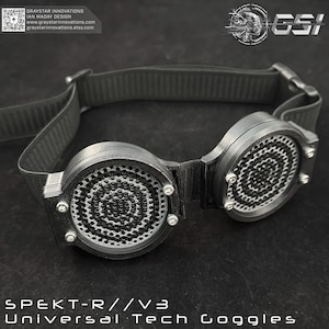 Puede incluir: Gafas de tecnología universal SPEKT-R//V3 negras con una correa negra ajustable. Las gafas tienen lentes circulares con un patrón en espiral y están aseguradas con pequeños tornillos plateados. El texto "SPEKT-R//V3 Universal Tech Goggles" está en la parte inferior.