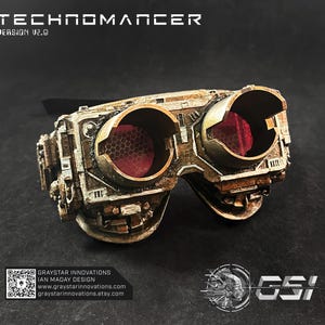 May include: Steampunk-style goggles with a metallic finish and red-tinted lenses. The goggles have a detailed, industrial design with the text "TECHNOMANCER" and "VERSION V2.0" at the top. The design includes the "GSI" logo and website information.