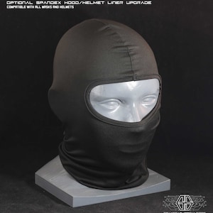May include: Black spandex balaclava with a single eye hole opening. The balaclava is on a gray stand. The text "OPTIONAL SPANDEX HOOD/HELMET LINER UPGRADE" is at the top of the image. The text "COMPATIBLE WITH ALL MASKS AND HELMETS" is below the first line of text. The text "GRAYSTAR INNOVATIONS" is at the bottom of the image.