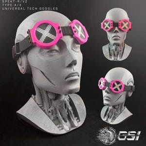 May include: Pink and black universal tech goggles with the text "SPEKT-R/V2 TYPE:A/X UNIVERSAL TECH GOGGLES". The goggles have a black strap and a white "X" design on the lenses. The goggles are displayed on a gray mannequin head.