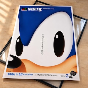 May include: A rectangular promotional poster for the video game Sonic the Hedgehog 3, featuring a large close-up of Sonic's blue and tan face. The text includes Sonic 3, 5月27日発売予定 5,800円, ソニック3もうすぐ発売, and the Sega Mega Drive 2 logo.