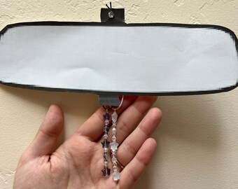 May include: Two strands of star-shaped beads hang from a rearview mirror. One strand is white and the other is purple.