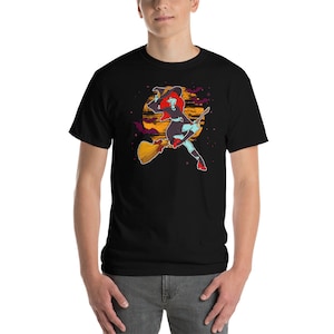 May include: A black t-shirt with a graphic of a witch flying on a broomstick in front of a full moon. The witch has red hair and is wearing a black dress and a witch's hat. There are bats flying around her.