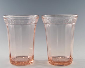 May include: Two clear pink glass tumblers with a delicate floral pattern around the rim. The glasses are empty and have a slightly flared shape.