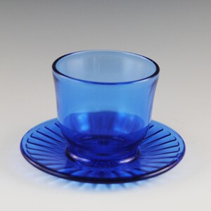 May include: A cobalt blue glass cup and saucer set. The saucer has a fluted design.