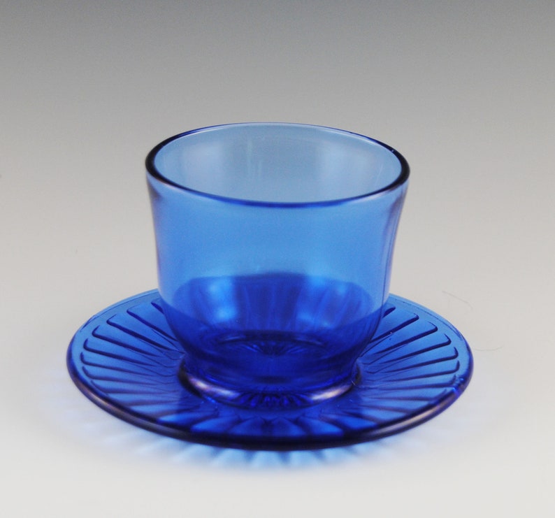 May include: A cobalt blue glass cup and saucer set. The saucer has a fluted design.
