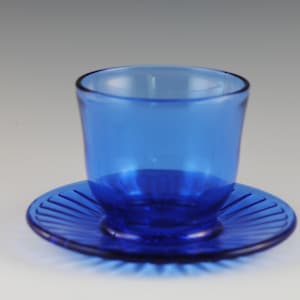 May include: A cobalt blue glass cup and saucer set. The saucer has a fluted design.