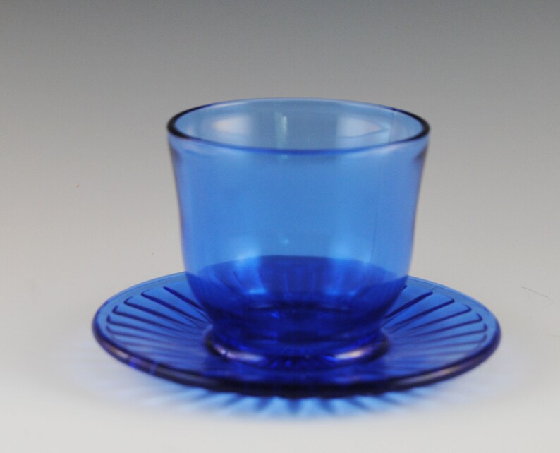 May include: A cobalt blue glass cup and saucer set. The saucer has a fluted design.