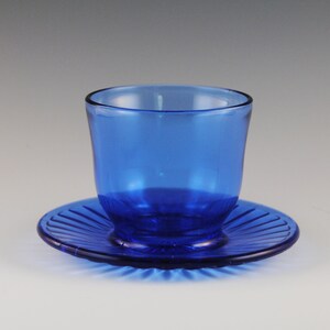 May include: A cobalt blue glass cup and saucer set. The cup has a rounded shape and the saucer has a fluted edge.