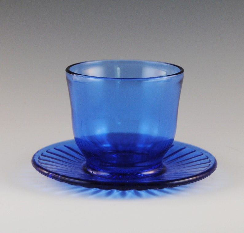 May include: A cobalt blue glass cup and saucer set. The cup has a rounded shape and the saucer has a fluted edge.