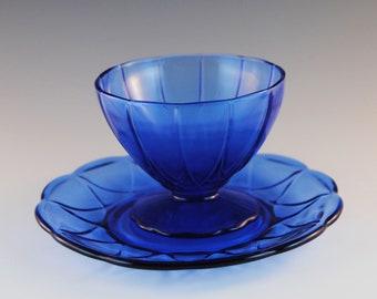 May include: A cobalt blue glass dessert dish with a scalloped edge and a matching saucer. The dish has a fluted design.