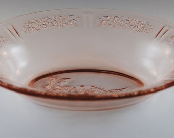 May include: A pink glass bowl with a floral design around the rim. The bowl is made of clear glass with a pink tint.