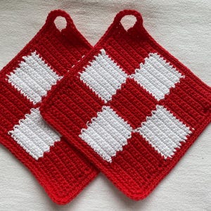 Può includere: Due presine a scacchi rosse e bianche all'uncinetto. Ogni presina ha una forma quadrata con un anello per appenderla. Il design presenta quadrati rossi e bianchi alternati, creando un motivo classico. Accessori da cucina fatti a mano.