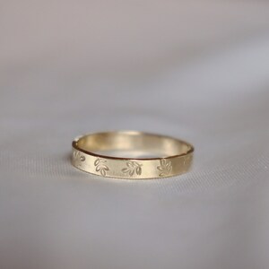 May include: A simple gold band ring with a delicate leaf pattern engraved around the band.