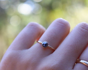 May include: A gold ring with a black gemstone set in a bezel setting. The ring is on a person's finger.
