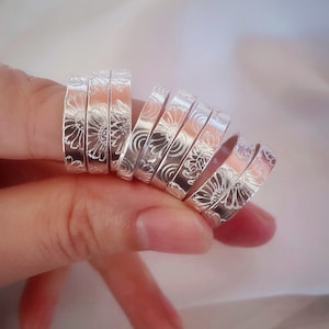 Op de afbeelding: Een set zilveren ringen met een bloemenmotief. De ringen zijn op elkaar gestapeld en worden aan een vinger gedragen.
