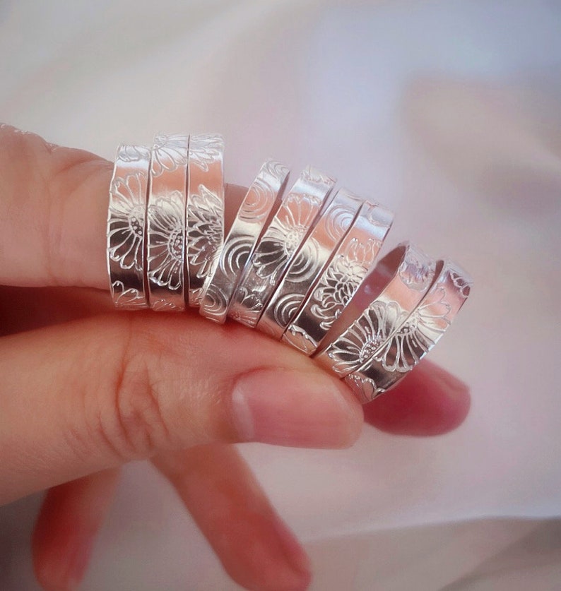 Op de afbeelding: Een set zilveren ringen met een bloemenmotief. De ringen zijn op elkaar gestapeld en worden aan een vinger gedragen.