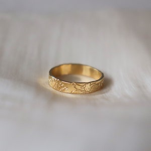 Op de afbeelding: Een gouden bandring met een bloemenmotief. De ring is simpel en elegant.