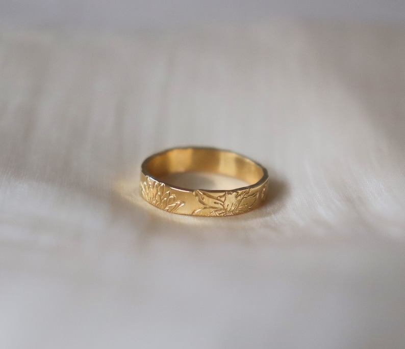 Op de afbeelding: Een gouden bandring met een bloemenmotief. De ring is simpel en elegant.