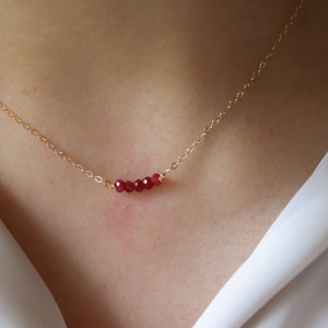 May include: A gold chain necklace with a row of small, dark red beads.
