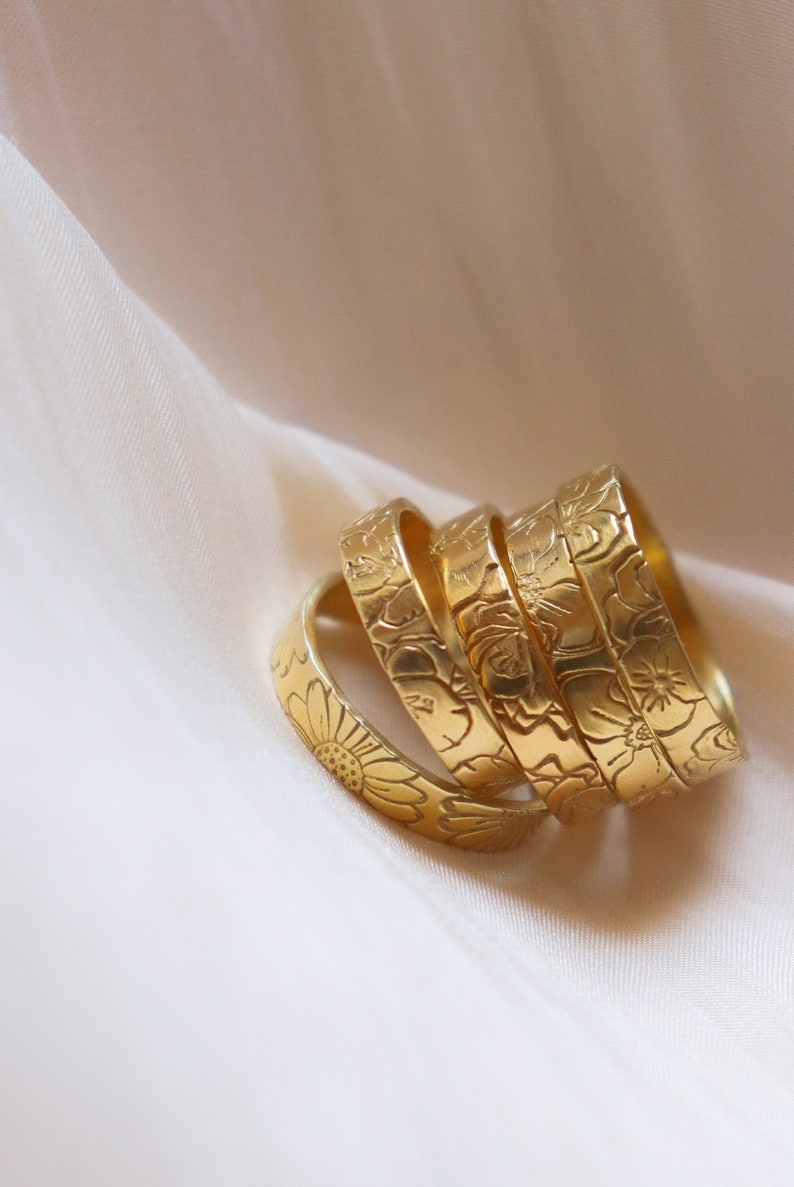May include: A set of four gold-toned rings with floral designs. The rings are stacked on top of each other, with the largest ring at the bottom and the smallest ring at the top.