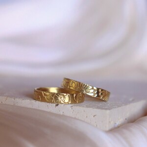 May include: Two gold rings with a floral design. The rings are stacked on top of each other.